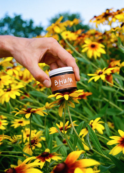 BHUM Whipped Tallow Balm Unscented - hand holding jar in flowers